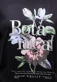 Svart skjorte med teksten "Botanical" over fargerike blomster og en sommerfugl, samt motiverende sitater om vekst og tankesett i hvit skrift.