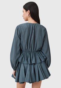 Abito peplum blu realizzato in tessuto leggero con maniche lunghe, vita arricciata e gonna a strati. La parte posteriore presenta un colletto rotondo e chiusura con bottoni.