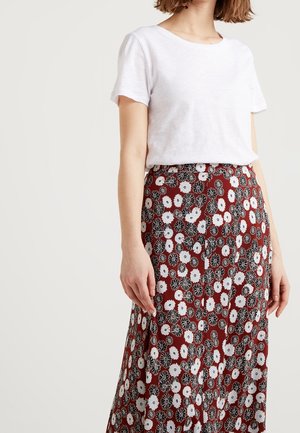 Kvinde iført en enkel hvid kortærmet skjorte indtucktet i et rødt nederdel med et hvidt og sort blomsterprint.