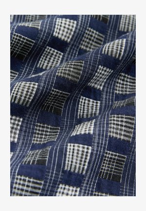 Jūros jėgos audinys su tekstūruotu langelių raštu balta ir juoda spalvomis. Minkšta, audinė medžiaga su matomais siuvimo detalėmis.