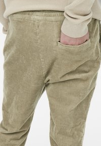 Pantaloni in corduroy beige con texture a righe verticali, vita elastica e tasca laterale, dal design comodo e rilassato.