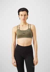 Sujetador deportivo verde oliva con logo negro, con tirantes finos y un diseño acolchado. Combinado con leggings negros de cintura alta.