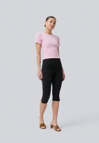 Fitted pink short-sleeve top with a round neckline, paired with black cropped leggings and brown heeled sandals on a light background.