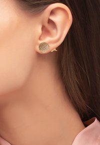 Orecchini a cerchio in oro con superfici rotonde e texture, arricchiti da una brillante impostazione a pavé. Accentuati da una piccola chiusura su un lato.