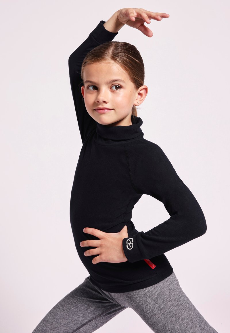 Zwart langemouwen coltrui met een aansluitend ontwerp en een logo-accent op de pols. Gecombineerd met grijze leggings, toont een dynamische pose.