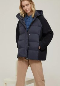 Giacca a vento blu navy con chiusura a zip e cappuccio, caratterizzata da un tessuto a maglia nero a contrasto sulle maniche e tasche laterali.