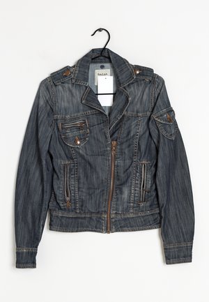 Veste en denim bleu foncé avec fermeture éclair devant, poches zippées et à boutons, et épaulettes suspendue sur un cintre noir sur fond blanc.
