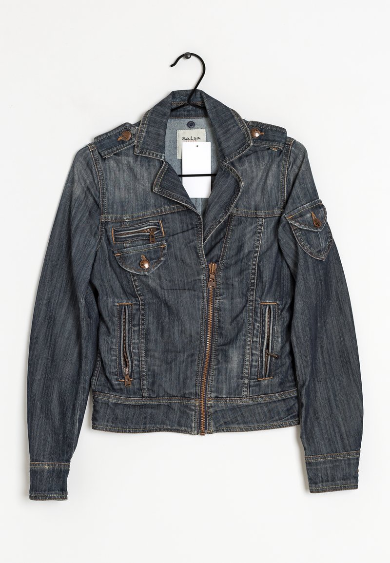 Veste en denim bleu foncé avec fermeture éclair devant, poches zippées et à boutons, et épaulettes suspendue sur un cintre noir sur fond blanc.