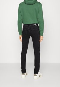 Vaqueros pitillo negros de talle alto, con bolsillos traseros y una pretina con marca, combinados con una sudadera verde y zapatillas blancas.