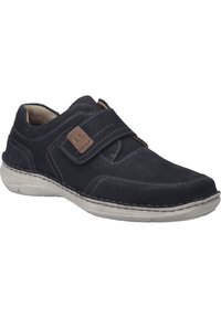 Schwarzer Wildlederschuh mit einem Klettverschluss, grauer Außensohle, kontrastierenden Nähten und einem gepolsterten Kragen für Komfort. Keine sichtbaren Muster oder Texturen.