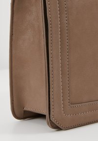 Brązowa skórzana torba o strukturalnym kształcie, z podwójnym przeszyciem wzdłuż krawędzi i gładką, teksturowaną powierzchnią.