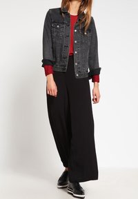 Veste en denim noire, haut rouge à manches longues, pantalon noir à jambes larges et chaussures noires à lacets. Caractéristiques : manches retroussées et textures contrastées.