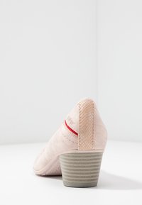 Růžová vysoká podpatková bota s texturovaným podpatkem a síťovaným designem. Obsahuje červený akcent na podpatku a hladký materiál na těle.