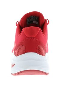 Red athletic shoe with a textured upper and mesh accents. Features a white sole and visible logo on the heel. Notable stitching detail.