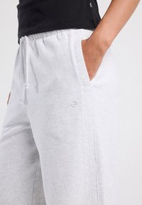 Valaiset harmaat collegehousut pehmeästä kankaasta, joissa on naru vyötäröllä, sivutaskut ja pieni logo-akkentti taskun lähellä.