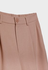 Pantalon beige taille haute avec fermeture par bouton, taille élastique à l'arrière, passants pour ceinture et texture de tissu lisse.