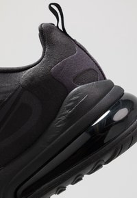 Gros plan sur le talon d'une chaussure de sport noire avec tissu texturé, languette de traction, semelle amortie et unité d'air visible sous le talon.