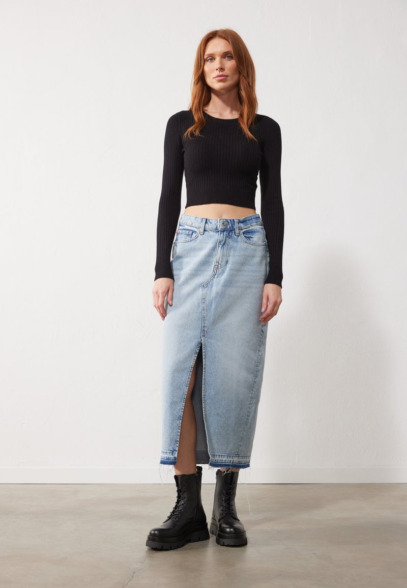 Lyseblå denimskjørt med en frontslitt, kombinert med en svart ribbet langermet crop top og svarte militærstøvler.