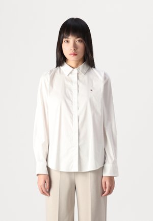 Camicia bianca con colletto classico, dotata di maniche lunghe e delicata ricamatura del logo sul petto. Tessuto liscio e leggero.