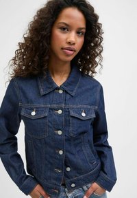 Tamsiai mėlynas džinsinis švarkas su sagų užsegimu, dviem krūtinės kišenėm ir apykakle. Pabrėžia sidabrines sagas ir kontrastingas siuvimo detales.