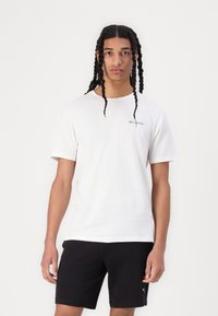Camiseta de algodón blanca con mangas cortas y cuello redondo, con un pequeño logo de Columbia en azul en la parte superior izquierda.