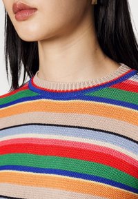 Sweter w paski z wielokolorowymi poziomymi liniami w czerwonym, zielonym, pomarańczowym, niebieskim i beżowym kolorze. Okrągły dekolt z teksturowanej dzianiny.