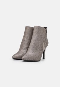Błyszczące brązowe botki za kostkę z wąskim czubkiem i obcasem typu stiletto, o gładkiej fakturze i subtelny czarny akcent przy obcasie.