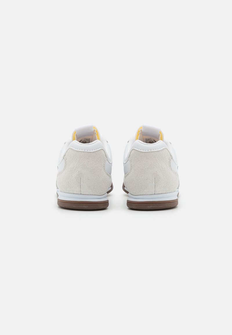 Vita sneakers med mockadetaljer vid hälen, brun gummisul, och vadderat ankelskydd. Utrustad med en dragflik för enkel påtagning.