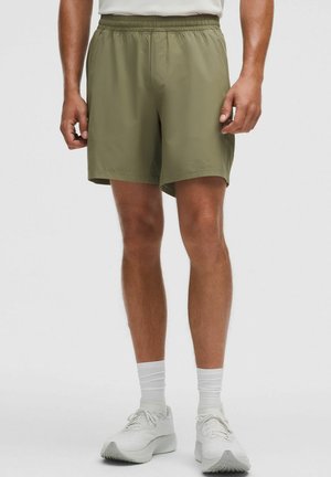 Pantalones cortos deportivos verde oliva con cinturilla elástica, tejido ligero y un ajuste relajado, combinados con zapatillas blancas y calcetines.