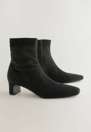 Bottines noires en suédine avec un bout pointu et un petit talon carré. Elles sont dotées d'une fermeture éclair sur le côté et d'une texture lisse.
