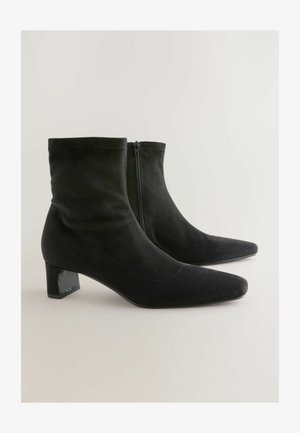 Botines negros de ante con punta afilada y un tacón cuadrado moderado. Cuentan con un zipper lateral y una textura suave.