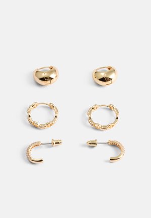 Ensemble de boucles d'oreilles dorées comprenant des créoles en forme de cœur, des créoles à maillons texturés, une simple puce et une pièce incurvée avec des accents clairs.