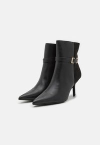 Les bottines noires présentent une combinaison de cuir lisse et de daim. Elles ont un design à bout pointu avec un talon stiletto fin et un accent décoratif avec une boucle.