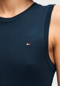 Σκούρο μπλε ριμπ τοπ χωρίς μανίκια με στρογγυλή λαιμόκοψη, που διαθέτει ένα μικρό κόκκινο, λευκό και μπλε λογότυπο στο αριστερό στήθος. Μαλακό βαμβακερό υλικό.