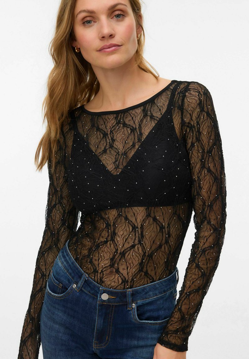 Svart blonder langermet body med et geometrisk mønster, med et solidt svart underlag og små hvite detaljer. Kombinert med blå jeans.