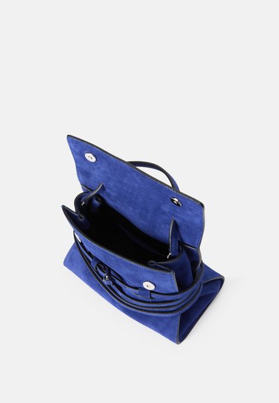 Μπλε σουέτ τσάντα με μαύρες δερμάτινες λεπτομέρειες, δύο χεράκια και μαγνητικό κλείσιμο. Ανοιχτή προοπτική που δείχνει το εσωτερικό με τσέπες και λείο ύφασμα.