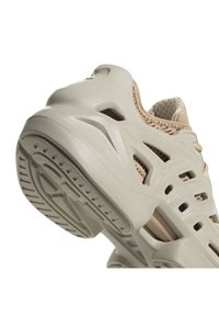 Vaaleanbeige tennari, jossa on teksturoitu, rei'itetty päällinen ja muotoiltu, paksu pohja, jossa on pitovoimakuviot ja leikkaukset tuuletusta varten.