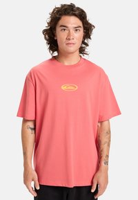 Koral kortärmad t-shirt i bomull, med en liten gul logotyp på bröstet, avslappnad passform och mjuk textur.