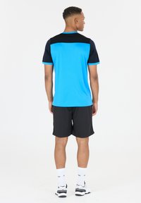 Blå tränings t-shirt med svarta axlar och turkosa detaljer, tillsammans med svarta shorts. Tillverkad av lätt, fukttransporterande material.