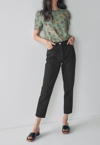 Blusa verde de flores de manga corta combinada con jeans negros de cintura alta y sandalias negras de plataforma con tacones de madera.