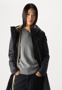 Schwarze gepolsterte Jacke mit Kapuze, über einem grauen Strickpullover getragen, der einen gerippten Saum und Bündchen aufweist; schwarze Hose; glatte Textur; neutrale Farben.