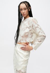 Witte kanten cropped top met bloemenmotief, lange mouwen, geschulpte zoom, doorschijnende stof, gecombineerd met een bijpassende textuurrijke rok.