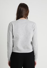 Sudadera gris con cuello redondo, puños y dobladillo acanalados, y un corte ligeramente cuadrado. Textura suave y diseño minimalista. Sin logotipo de marca visible.