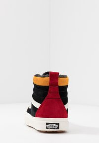 Hoge sneakers met een zwart suede bovenwerk, rode en gele accenten, witte strepen en een crèmekleurige rubberen zool. Voorzien van een gewatteerde kraag en logo.