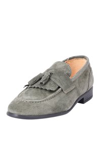 Mocassini in suede verde con tacco piatto nero, caratterizzati da dettagli di frange e nappine sulla parte anteriore. Rivestimento interno liscio.