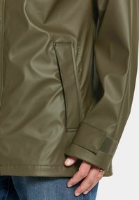 Olivgrön vattentät jacka med en slät, glänsande yta, en sidoficka med tryckknapp och en ärm med kardborrejustering.