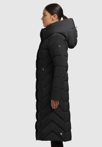Fekete puffkabát, chevron mintázattal, hosszú fazonnal, kapucnival és oldalsó cipzáros zsebekkel. Az ujjon logós címke található. Sima textúrájú.