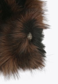 Vêtement en fausse fourrure présentant un dégradé de brun foncé et de noir, avec une surface texturée et un accent décoratif métallique.