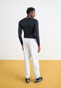 Tricou negru cu mânecă lungă, ajustat, cu textură netedă și guler rotund, asortat cu pantaloni cargo gri deschis și adidași negri.