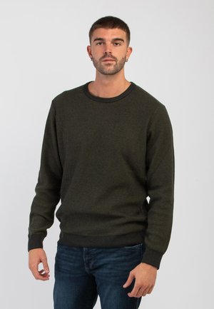 Maglione verde scuro a trama con colletto rotondo e maniche lunghe, abbinato a jeans in denim blu. Il tessuto presenta un motivo sottile.